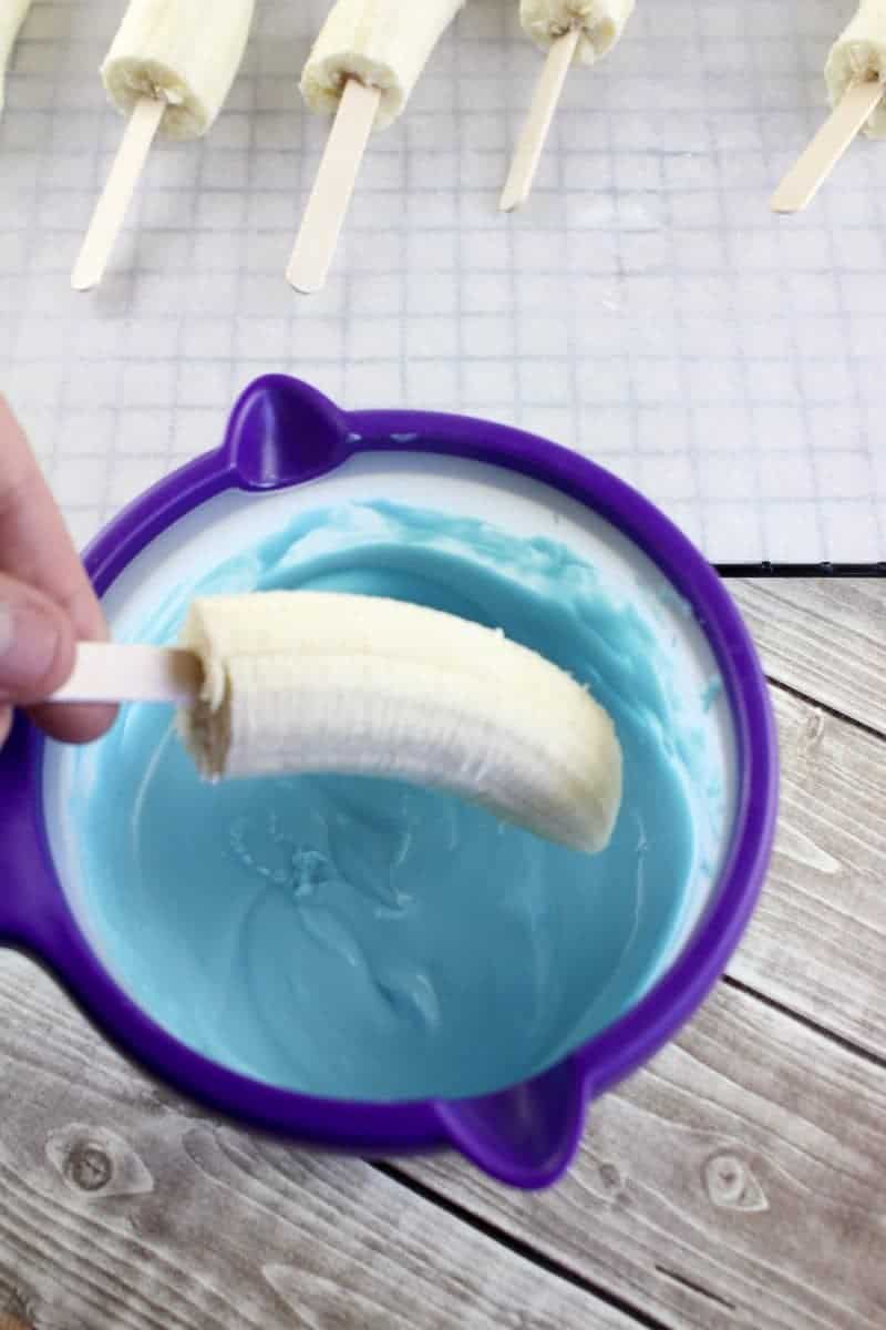 Bananas being dipped into melted blue candy.