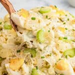 Wooden spoon lifting a spoonful of creamy potato salad.