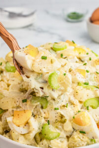 Wooden spoon lifting a spoonful of creamy potato salad.