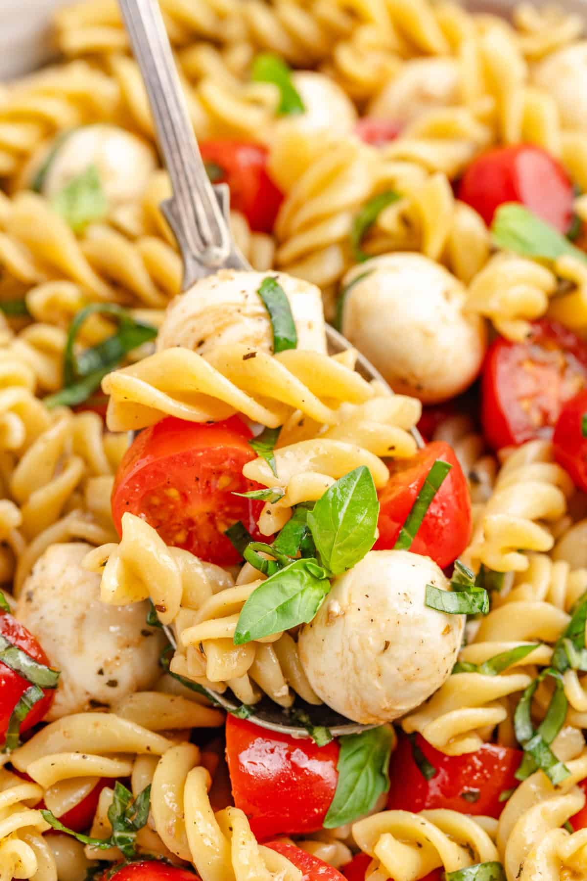 Close-up of a fork lifting a bite of caprese pasta salad with tomato, mozzarella, and basil.