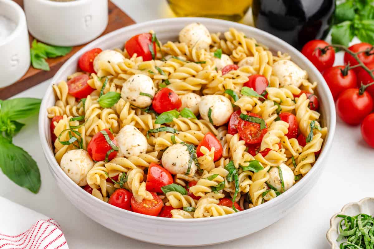 Bowl of pasta caprese salad with tomatoes and mozzarella, photographed from the side.
