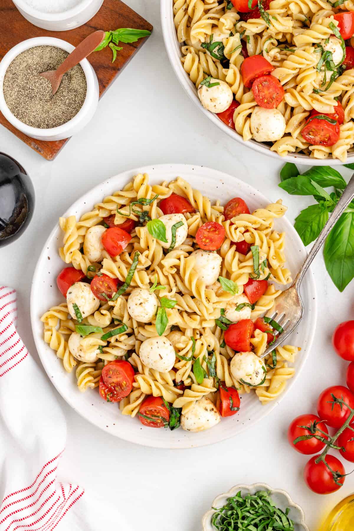 Bowl of rotini pasta salad with cherry tomatoes, mozzarella balls, and basil.