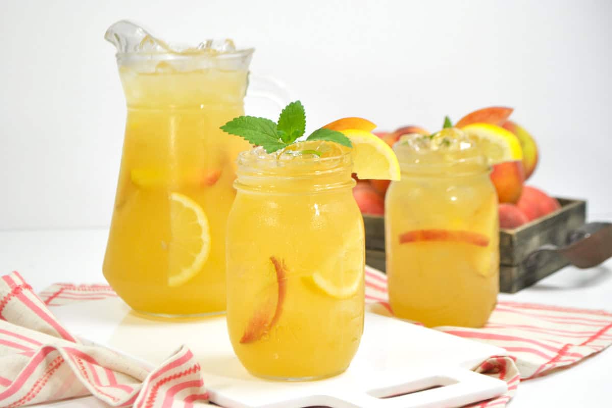 A mason jar of homemade peach lemonade with lemon and peach slices, garnished with mint and lemon.