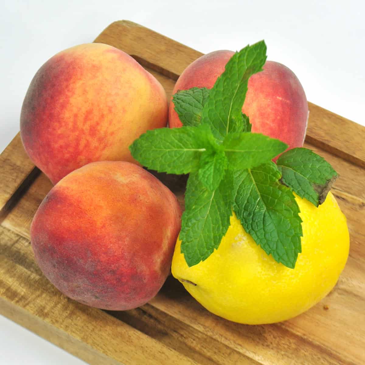 Fresh peaches, a lemon, and mint sprig on cutting board.