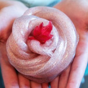 A cinnamon-scented fall slime with glitter in a child's hands with a small red plastic leaf toy on top of it.