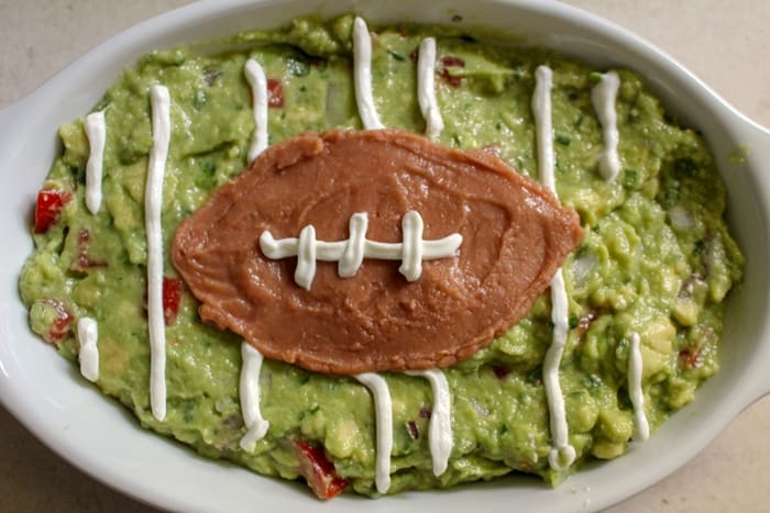 Spoon sour cream into a plastic baggie and cut a very small hole in the corner. Use baggie to pipe sour cream onto guacamole to make yard lines. 