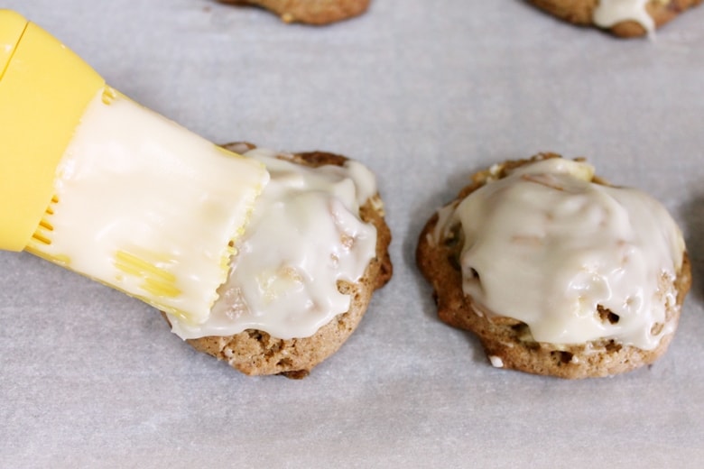 Brushing vanilla glaze on warm soft apple cookies