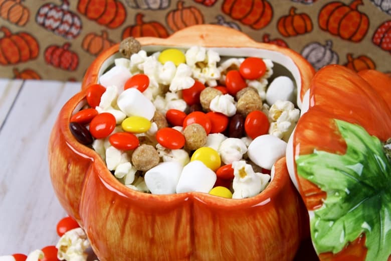 No bake fall snack mix with mini marshmallows, kettle popcorn, Reese's pieces, and Reese's Puffs Cereal served in a pumpkin shaped bowl.