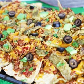 Loaded nachos on a sheet pan topped with cheese, beef, olives, cilantro, and avocado.