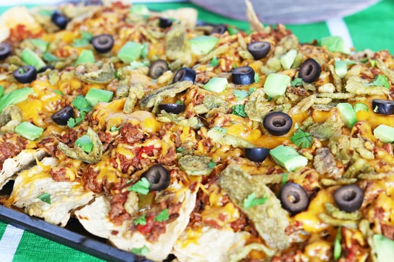 Loaded nachos on a sheet pan topped with cheese, beef, olives, cilantro, and avocado.