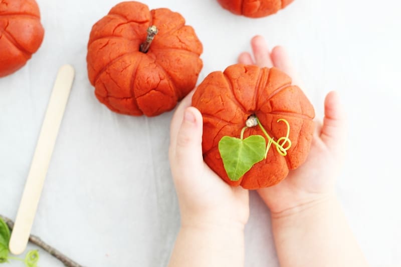 Child holding pumpkin spice playdough formed into a pumpkin