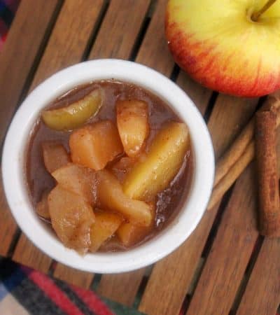 cinnamon fried apples in a bowl next to an apple and cinnamon sticks