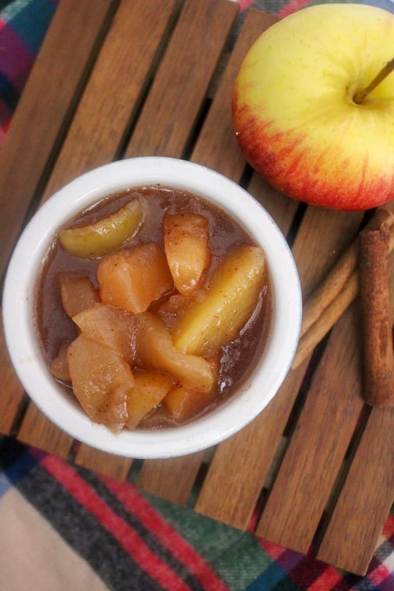 cinnamon fried apples in a bowl next to an apple and cinnamon sticks