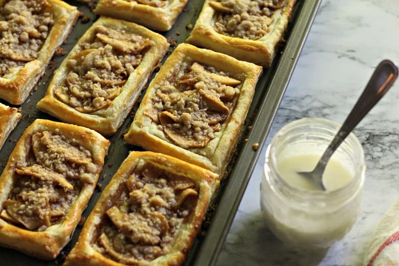 Apple Danishes on baking sheet with icing in jar next to them