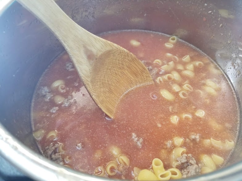 Instant Pot filled with macaroni, beef, broth, tomato puree and spies.