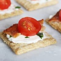 Triscuit crackers with cream cheese, bacon, and tomato on a platter