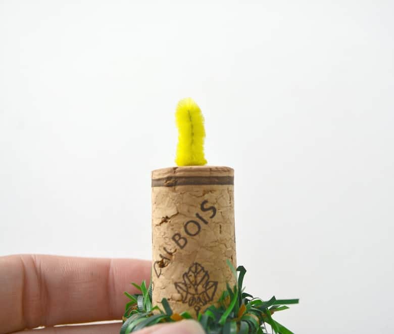 yellow pipe cleaner made to look like a flame on top of a wine cork wrapped with garland