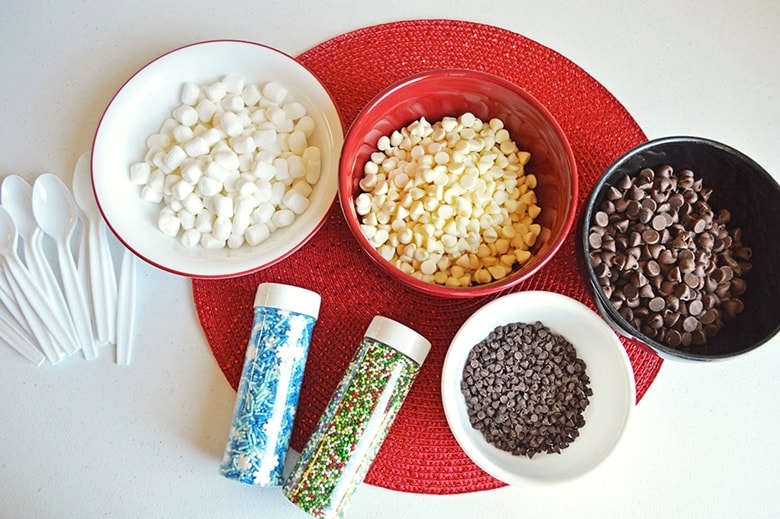 Bowls of mini marshmallows, white chocolate chips, chocolate chips, mini chocolate chips, and various sprinkles 