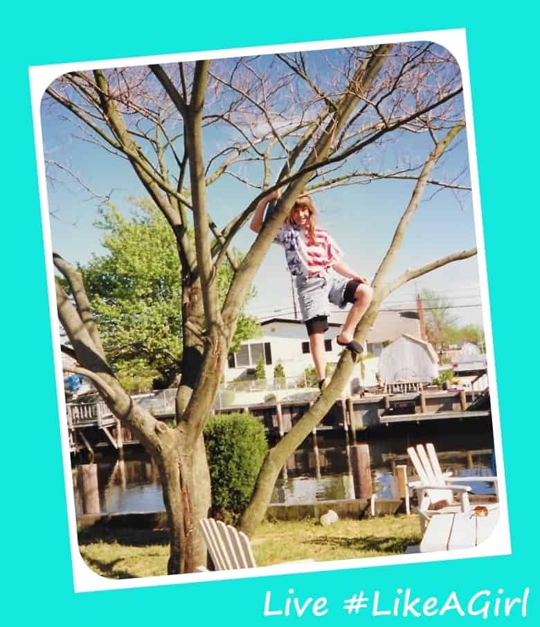 Young girl, about age 10, climbing on a tree branch in a backyard.