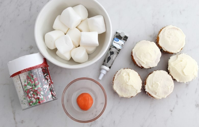 Melting Snowman Cupcakes Ingredients: iced cupcakes, orange fondant, marshmallows, black decorating gel, and sprinkles