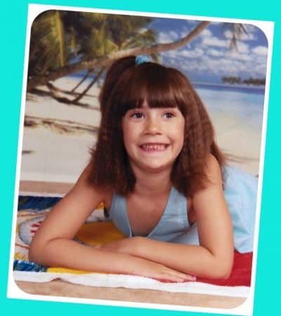 Young girl in a blue sundress, smiling and posing on a towel on the beach.