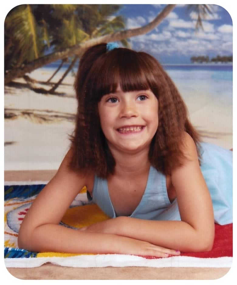 Young girl in a blue sundress, smiling and posing on a towel on the beach.