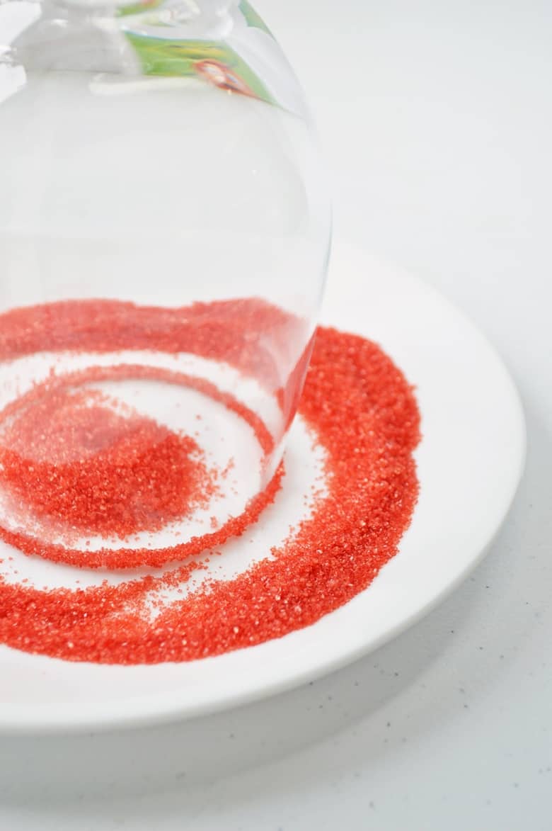 Upside-down wine glass being dipped in red sanding sugar.