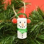 Wine cork decorated to look like a snowman hanging on a christmas tree.