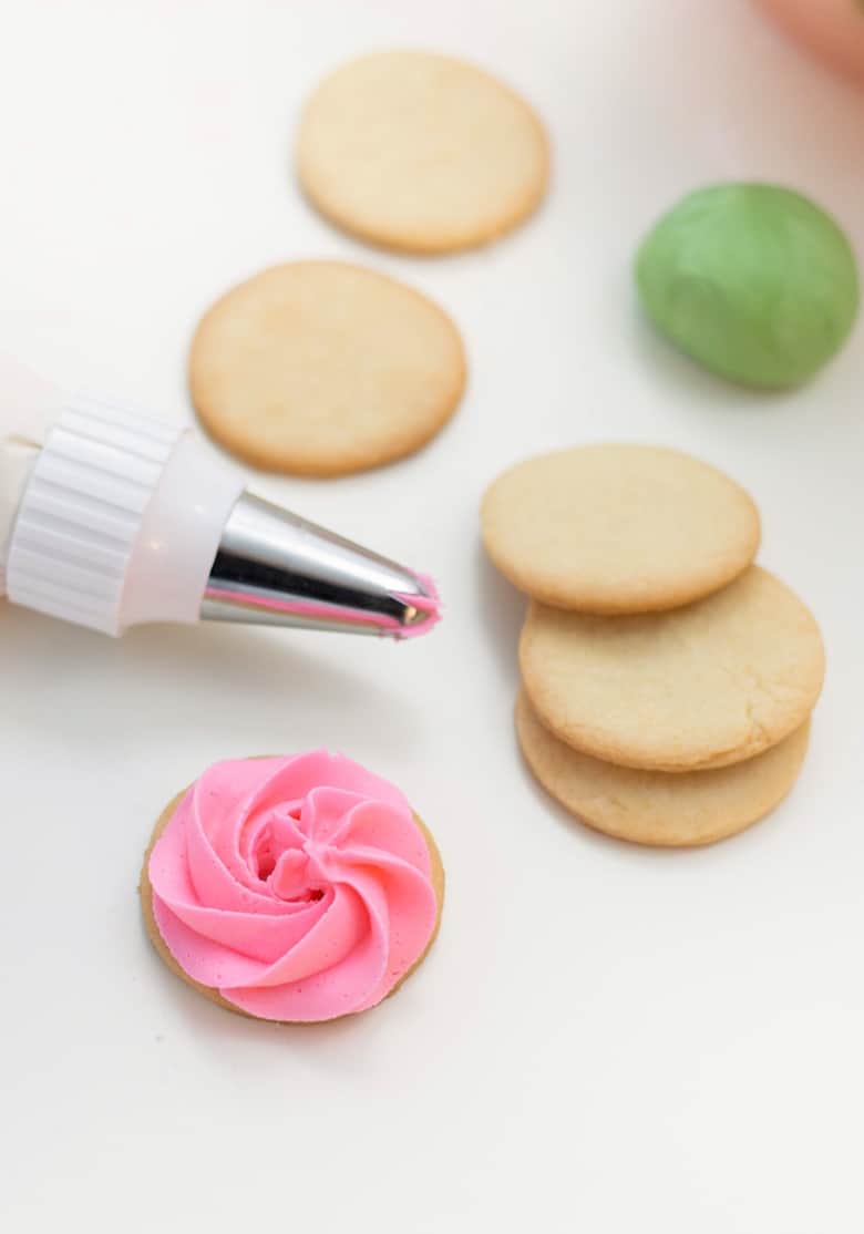 Piping pink buttercream icing onto round sugar cookies