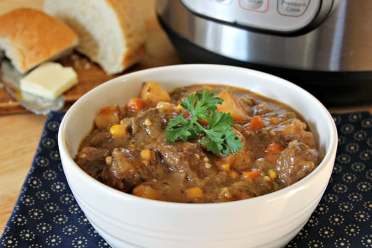 Bowl of beef stew on a navy blue placemat with french bread and an Instant Pot in the background.