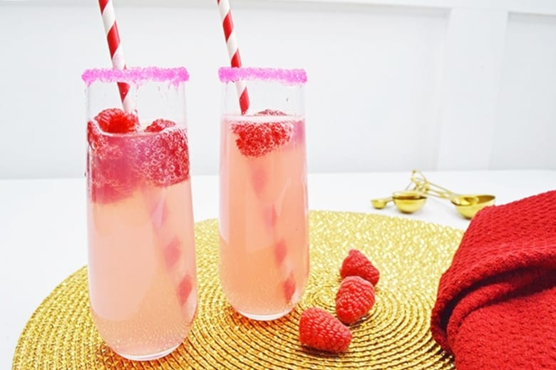 Tasty Raspberry Lemonade Mimosa cocktail in a tall glass with pink sugared rim and fresh raspberries.