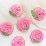 sugar cookies decorated to look like roses using pink icing and green fondant