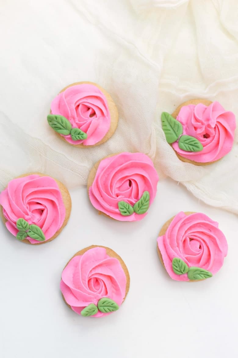 sugar cookies decorated to look like roses using pink icing and green fondant