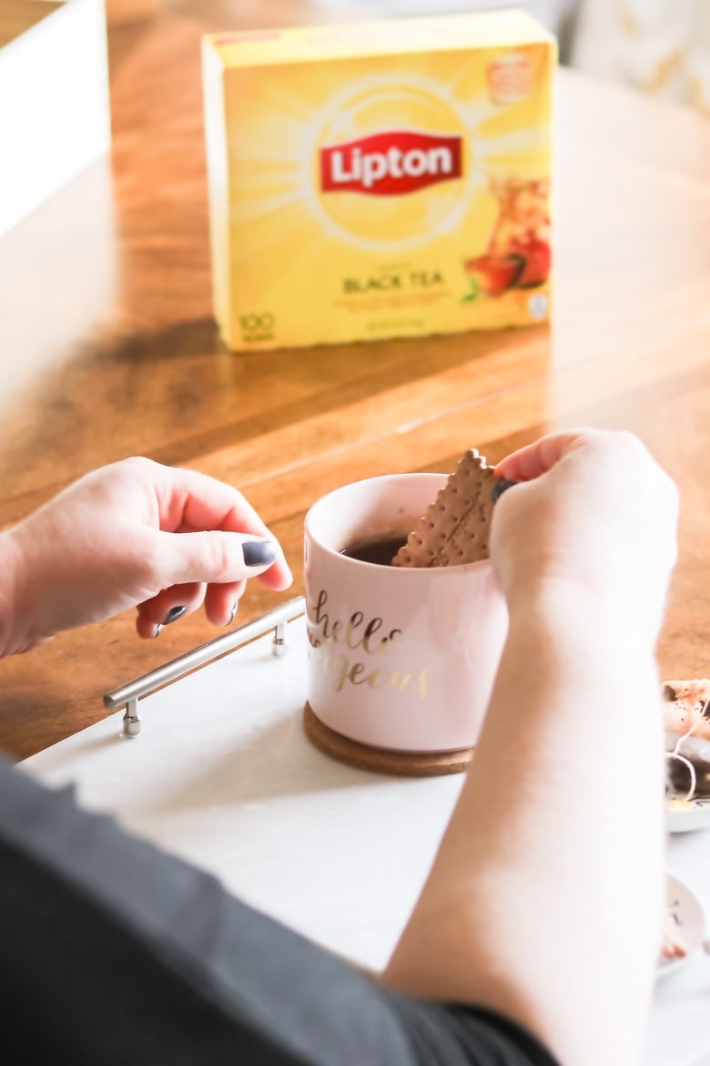 dunking a tea biscuit in a mug of Lipton Black Tea. The box of Lipton Tea is in the background.