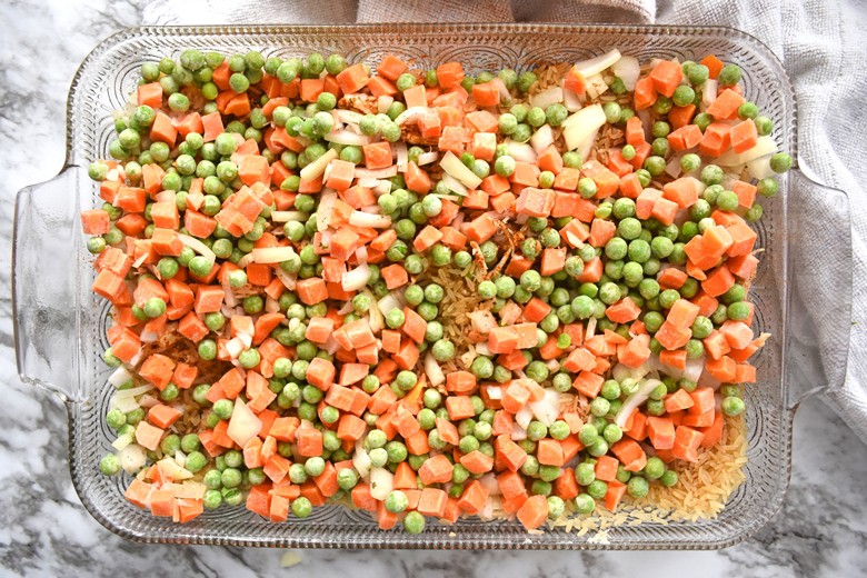 chicken, rice, frozen peas and carrots, and chopped onions in baking dish