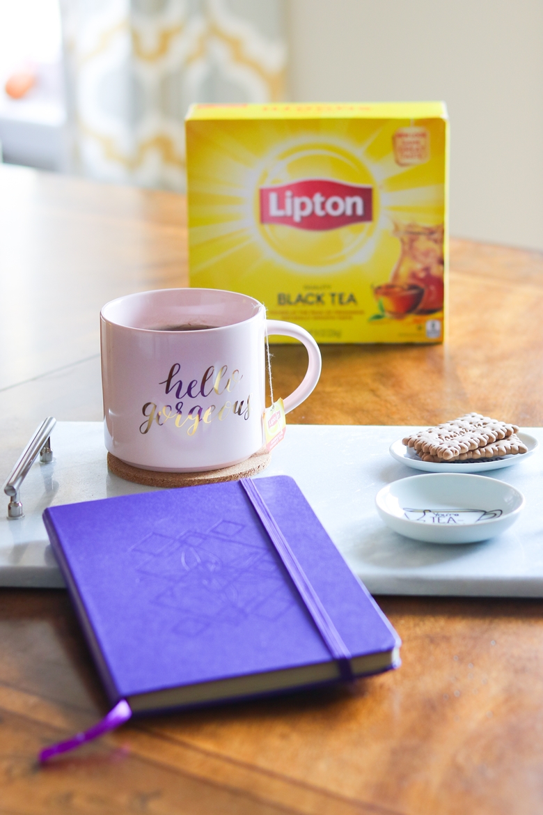 Hello Gorgeous pink coffee mug, purple notebook, and tea biscuits on a tray with a box of Lipton tea in the background.