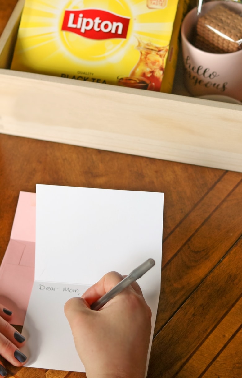 someone handwriting a card, with a tea gift basket in the background