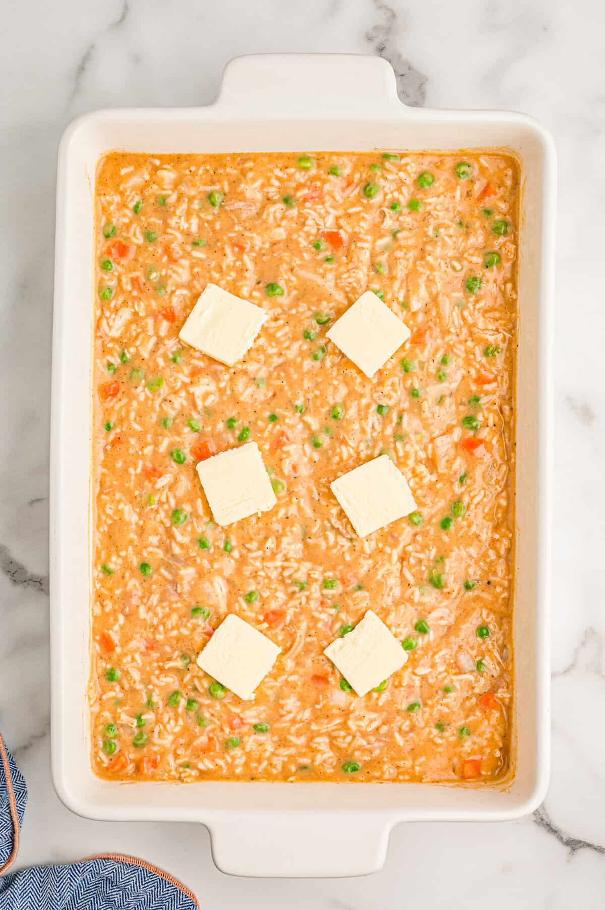 Six slices of butter placed across the top of the unbaked casserole in the dish.