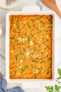 The finished baked casserole in a white dish with a serving plate and wooden spoon nearby.