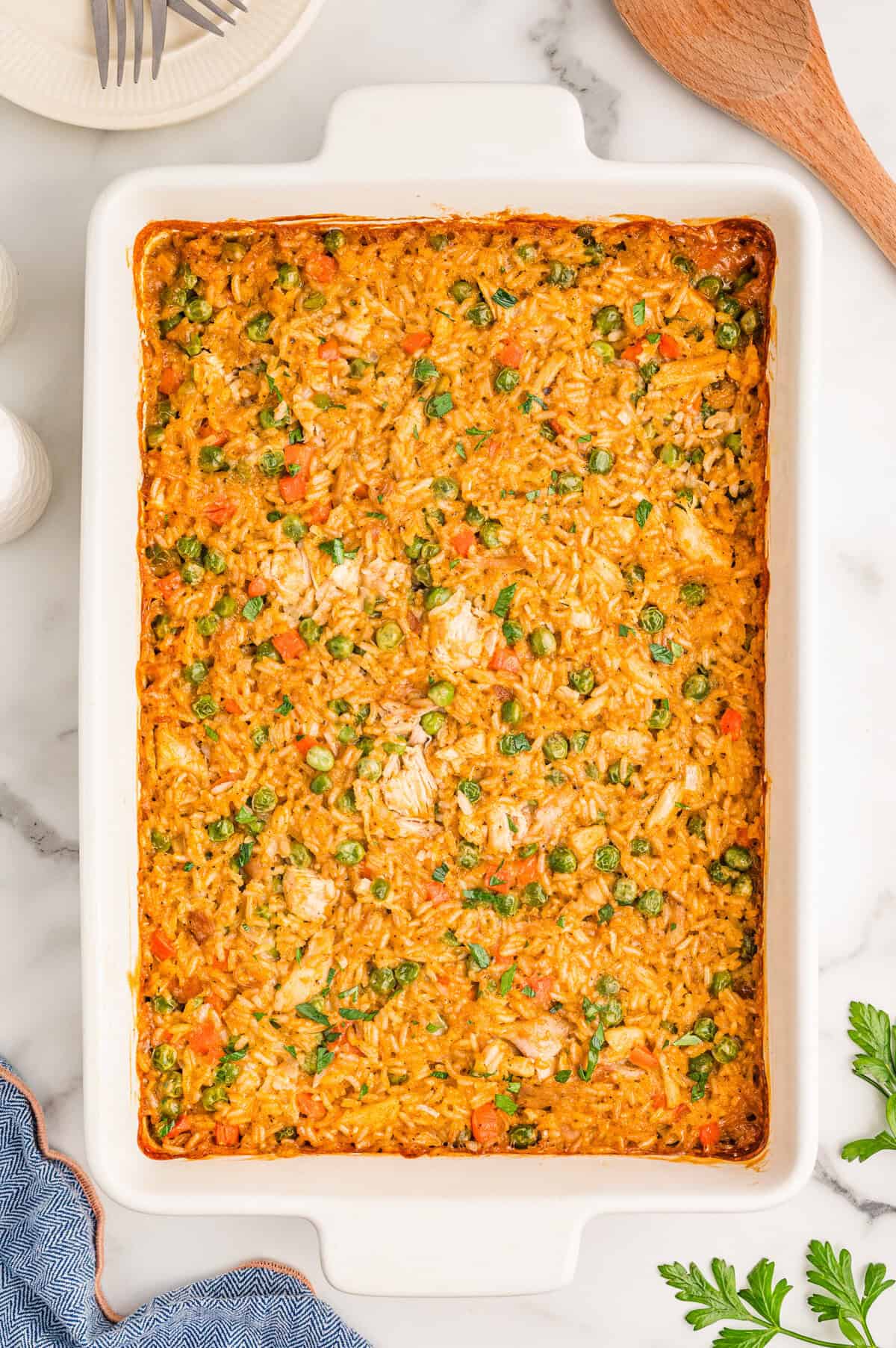 The finished baked casserole in a white dish with a serving plate and wooden spoon nearby.