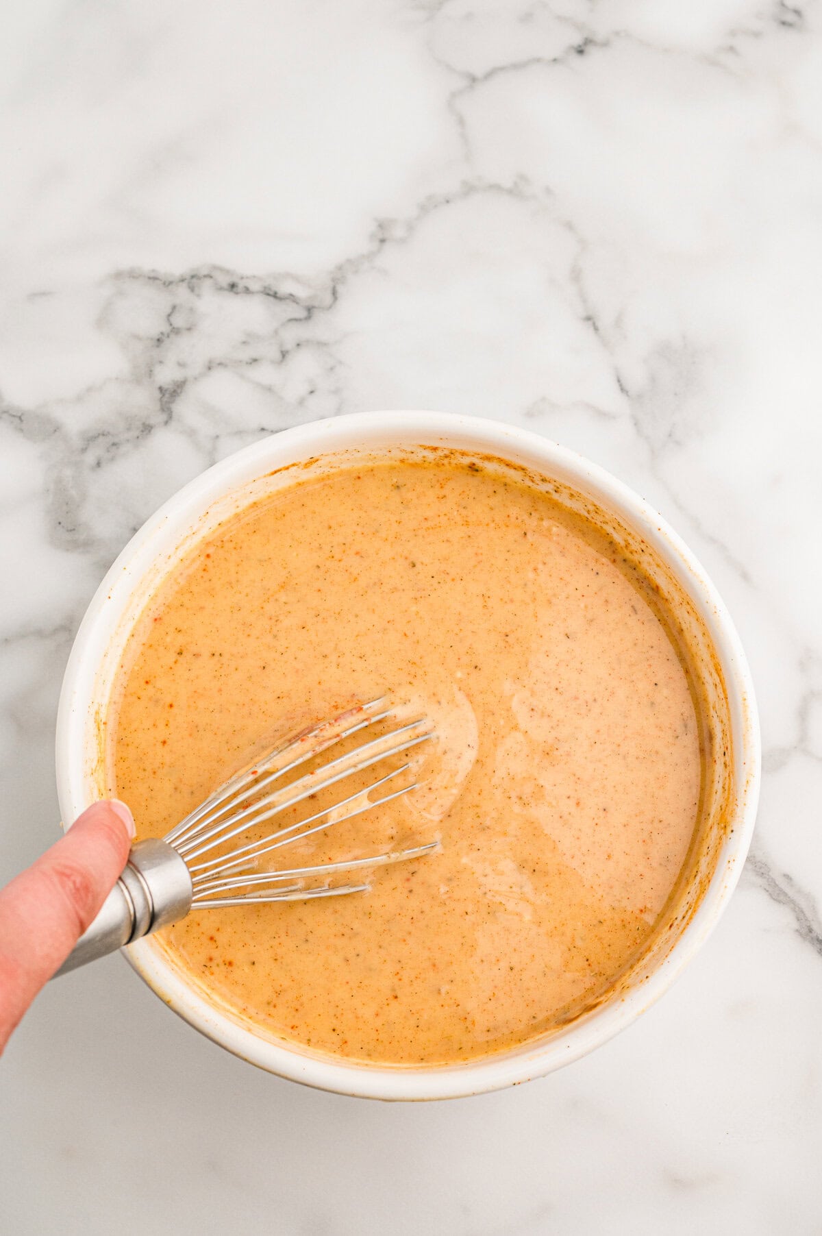 A creamy orange soup mixture being whisked in a white bowl.