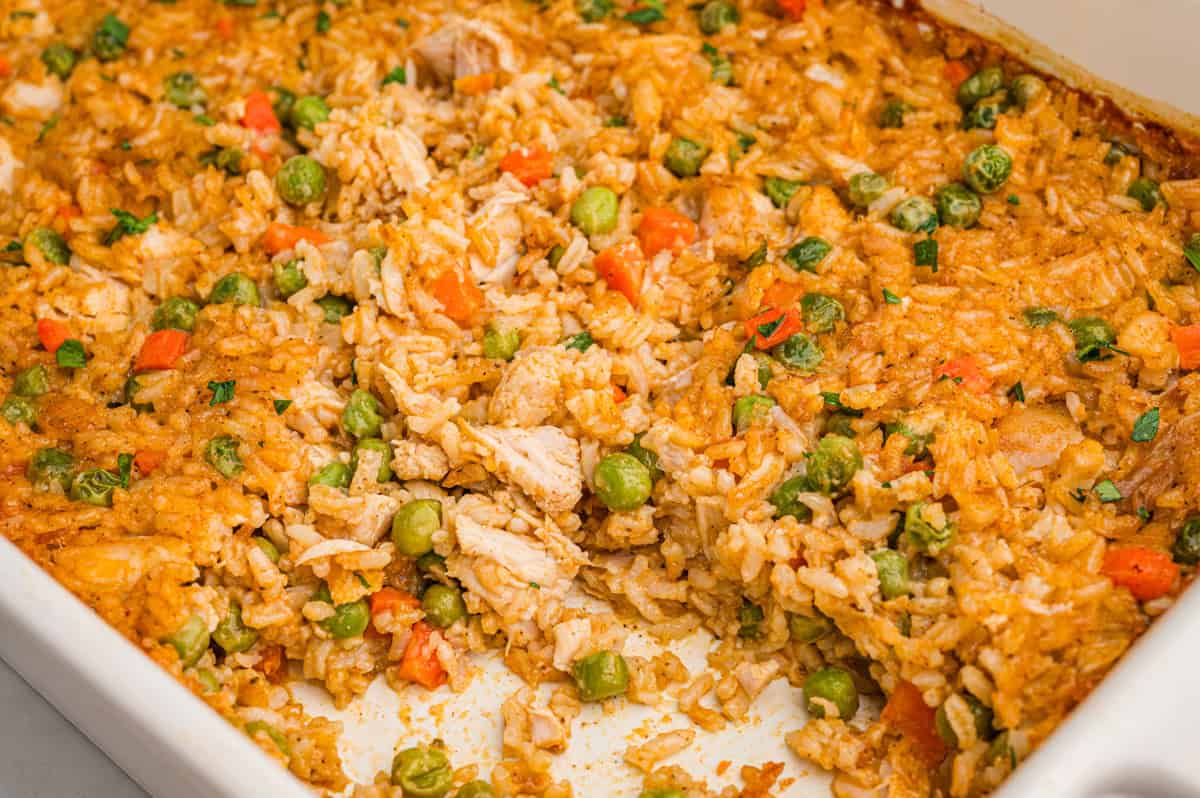 Chicken and rice casserole baked in a white dish with peas, carrots, and parsley.