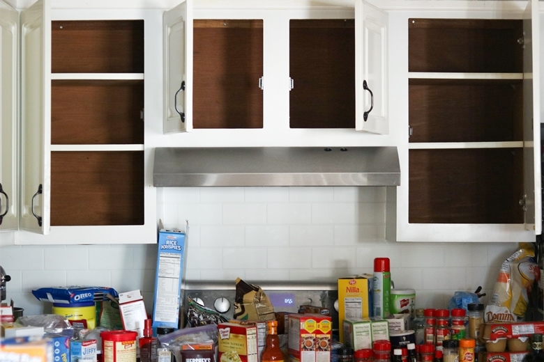 Empty cabinets with a lot of pantry items removed and placed on countertop underneath