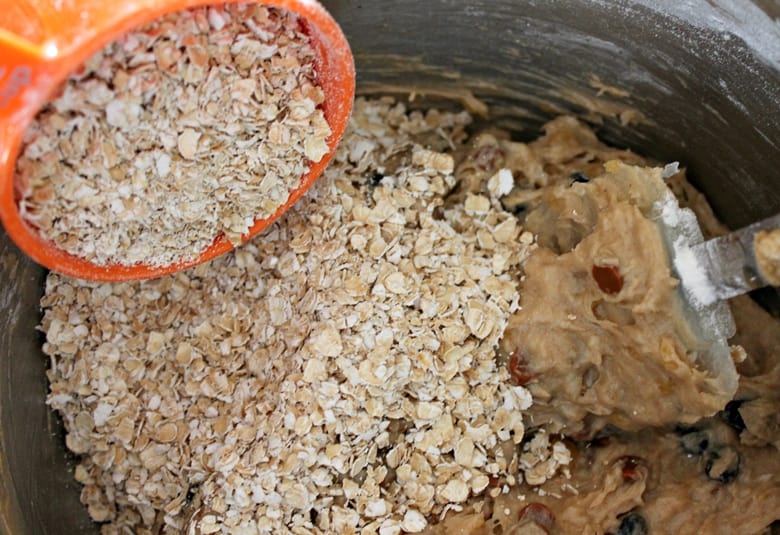 Pouring oats into cookie batter in stainless steel bowl