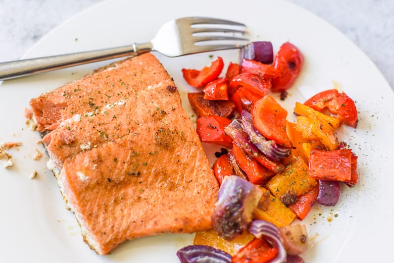 Salmon filet, peppers, and onions on a white plate with a fork.