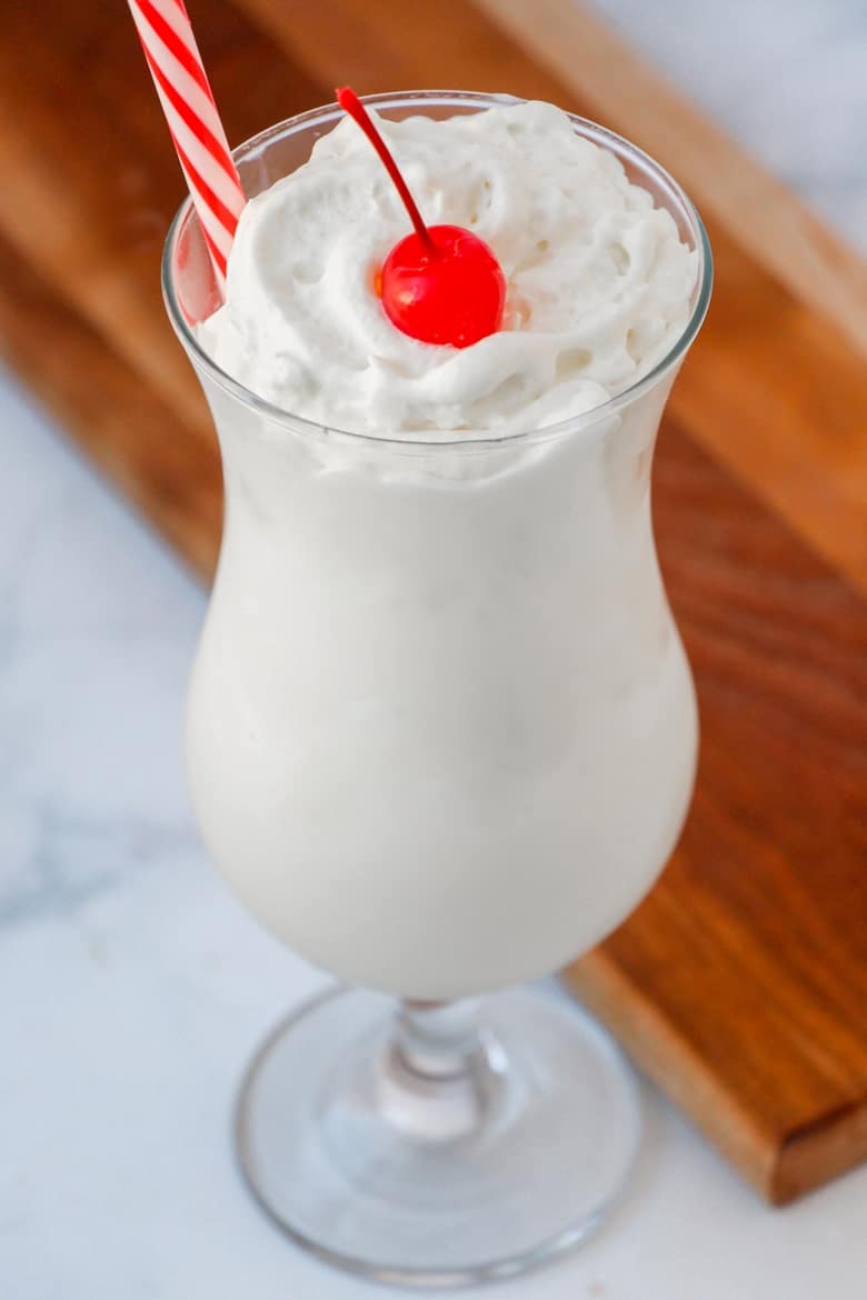 Vanilla frozen drink in a clear glass with a cherry on top and a straw.