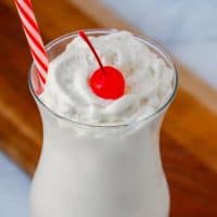 Vanilla frappe in a glass with a cherry on top and a red and white striped straw.