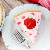 Slice of Strawberry Jello Pie on white plate, garnished with whipped cream and strawberries