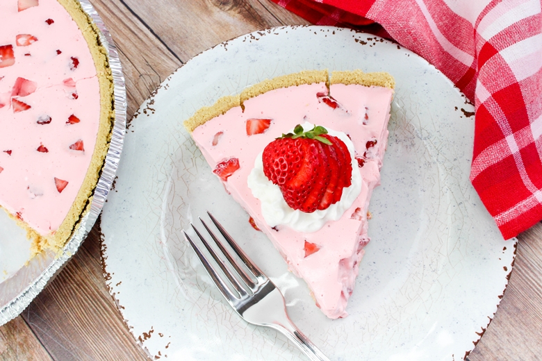 Slice of Strawberry Jello Pie on white plate, garnished with whipped cream and strawberries