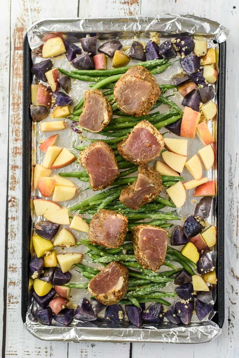Uncooked pork tenderloin medallions with veggies on a sheet pan